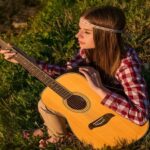 Como aprender a tocar violão sozinho? Garota sozinha em meio à natureza segurando um violão de cordas de nylon, transmitindo tranquilidade e inspiração musical.