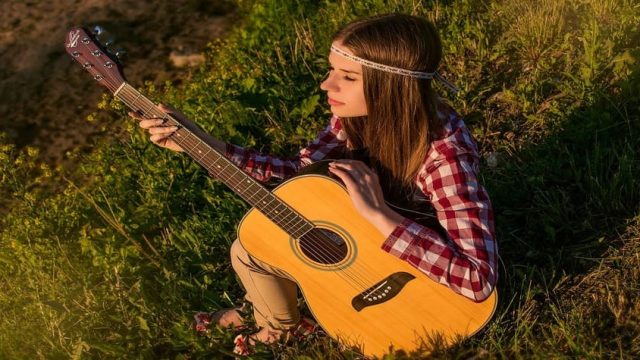 Como aprender a tocar violão sozinho? Garota sozinha em meio à natureza segurando um violão de cordas de nylon, transmitindo tranquilidade e inspiração musical.