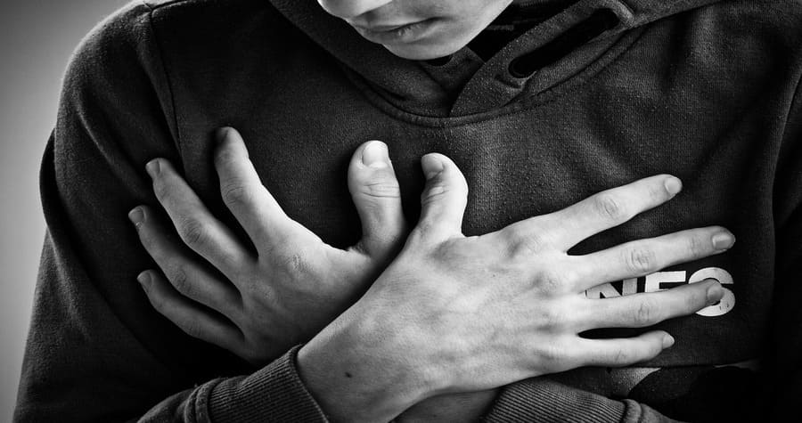Ansiedade não é falta de fé: pessoa com as duas mãos no peito, em sinal de desespero durante uma crise de ansiedade, representando sofrimento emocional e angústia